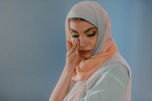 A woman wearing a hijab wiping the tears off her face.