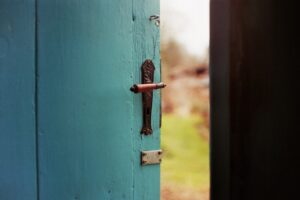A stock photo that shows a partially open aqua colored door, with a glimpse of the outdoors beyond.