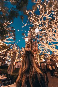 A woman walking through an outdoor square lit up with holiday lights.